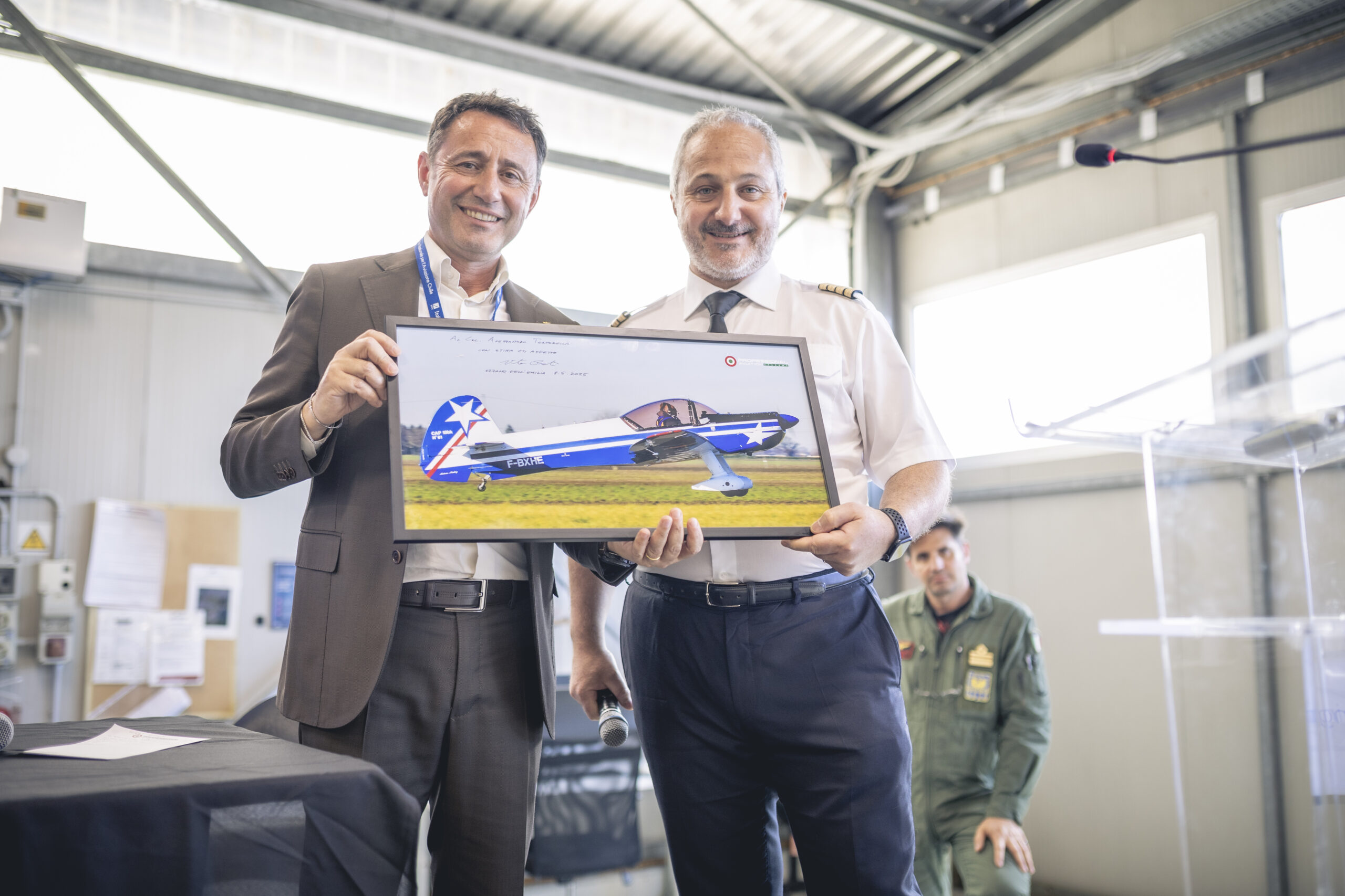 “Col. Alessandro Tortorella and Capt. Vito Preti hold a framed photo of an aerobatic aircraft during a presentation at Professional Aviation "Col. Alessandro Tortorella and Capt. Vito Preti hold a framed photo of an aerobatic aircraft during a presentation at Professional Aviation
